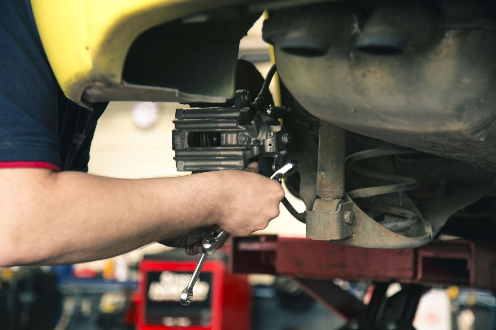 A mechanic working underneath a raised car with a spanner